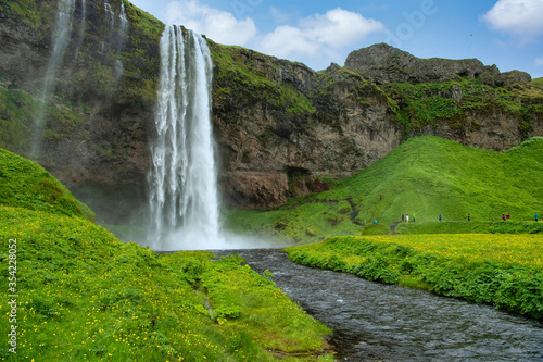 Panoramic view of valley and waterfall Seljalandsfoss in Iceland Many tourists follow the path to see the back of the waterfall. In the summer  there are yellow grass and wildflowers.