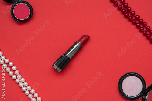 Fototapeta Naklejka Na Ścianę i Meble -  Red lipstick, white and red beads, red and pink eye shadows on a red background