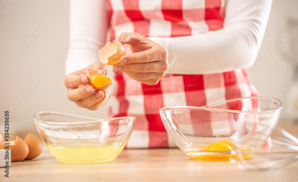Detail of woman's hands separating egg yolks from the whites into two glass bowls