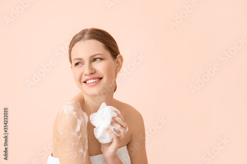 Beautiful young woman taking shower on color background