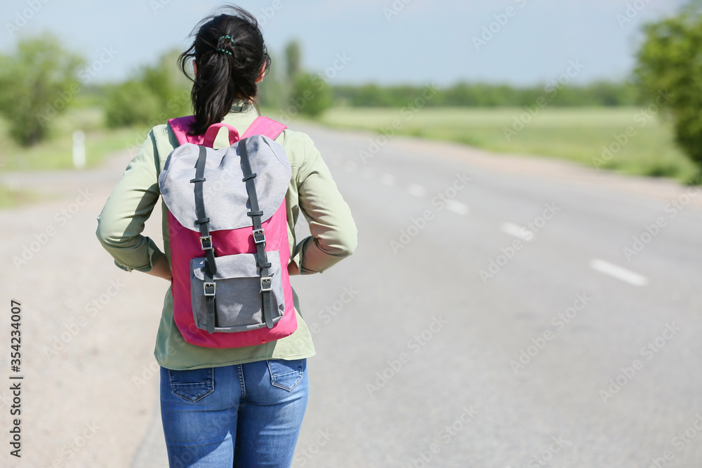Female traveler with backpack walking along the road