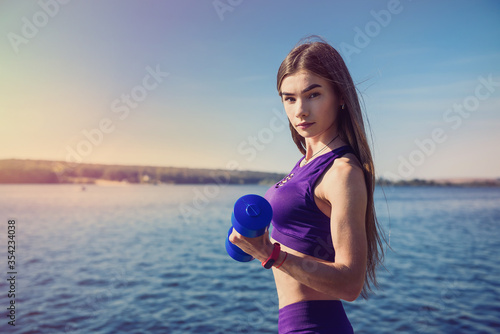 Young fit woman in sportswear doing morning exercise with dumbbells outdoors. healthy lifestyle.