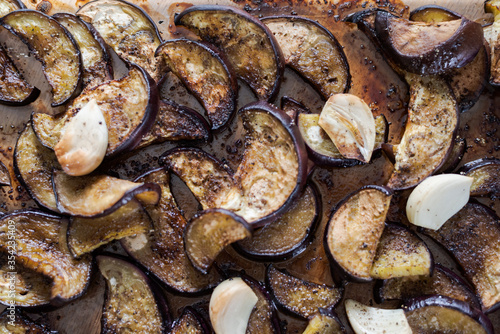 Sliced eggplants baked in oven with garlic cloves lying on glass tray ready to be eaten