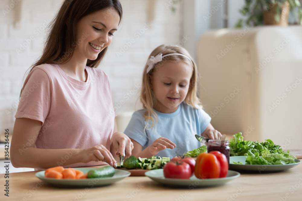 Caring young mother have fun chop vegetables preparing salad with cute little daughter at home, loving mom or nanny cooking breakfast together with small preschooler girl child in cozy kitchen Caring young mother have fun chop vegetables preparing salad with cute little daughter at home, loving mom or nanny cooking breakfast together with small preschooler girl child in cozy kitchen