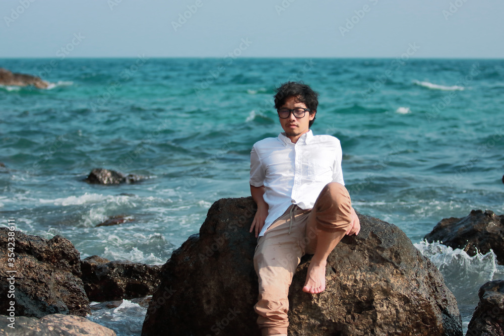 Relaxed handsome young Asian man sitting at seashore in vacations weekend.