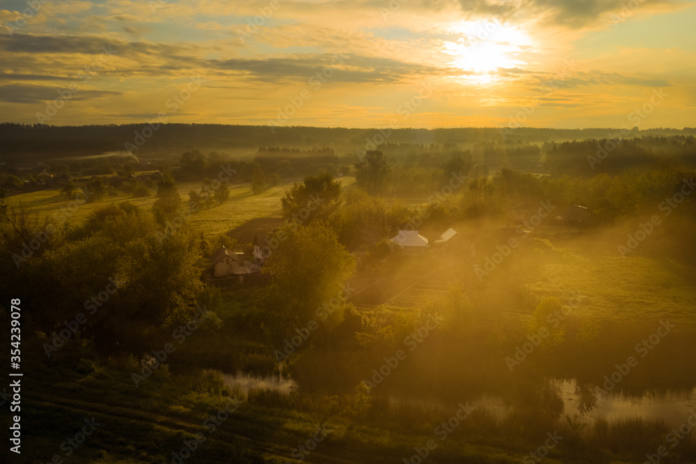 Golden orange mist over the village. Dramatic morning landscape with fog, river and meadow in the golden hour at dawn. 