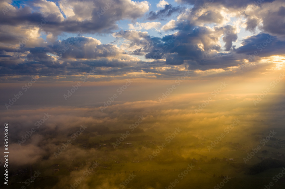 Fototapeta premium aerial view of Beautiful summer foggy nature landscape. Tranquil morning scene with foggy hollow and amazing clouds in sky during sunrise.Farm fields and green hills at sunrise.