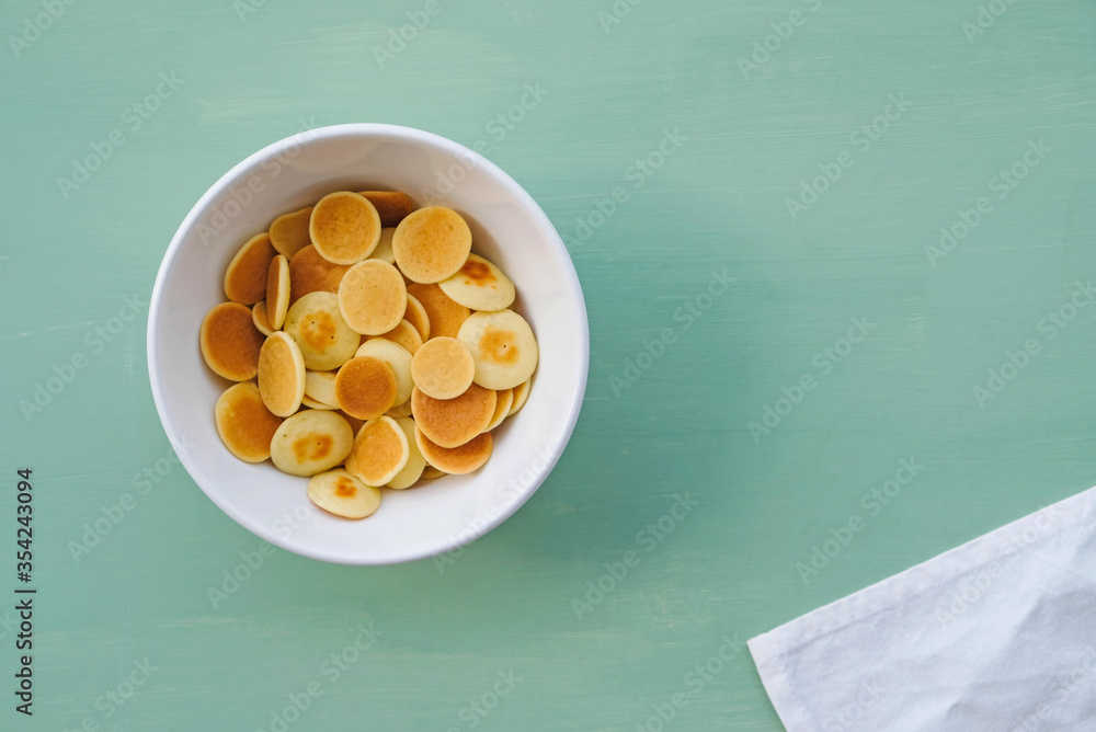 Freshly cooked pancake cereal in a bowl on mint green background. Freshly cooked pancake cereal in a bowl on mint green background.