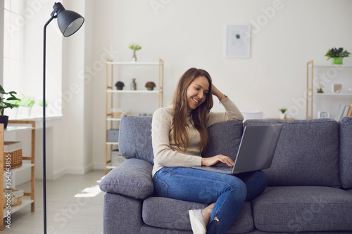 Online chat. Young woman works with a laptop using a web video camera while sitting on a sofa in a room.
