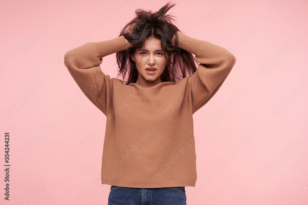 Indoor photo of young pretty brown haired woman cluthing her head with raised hands and looking attentively at camera, isolated over pink background Indoor photo of young pretty brown haired woman cluthing her head with raised hands and looking attentively at camera, isolated over pink background