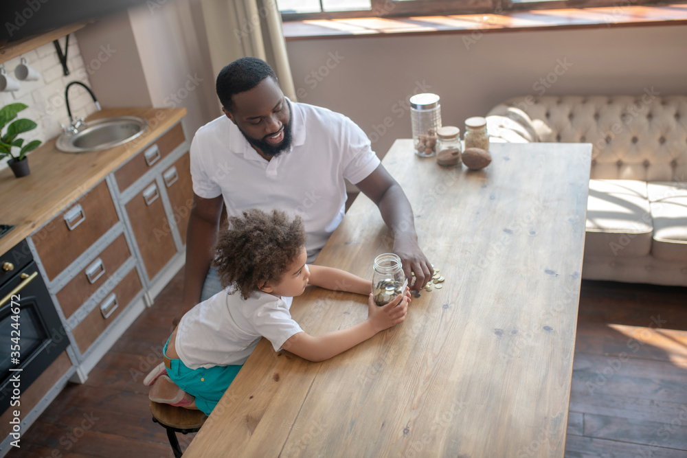 Dark-skinned bearded man talking to his son about saving money Dark-skinned bearded man talking to his son about saving money