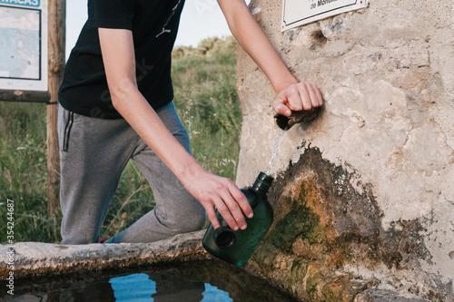 Teen hiker filling a bottle of water at a spring in the countryside during a water drink break. Selective focus.