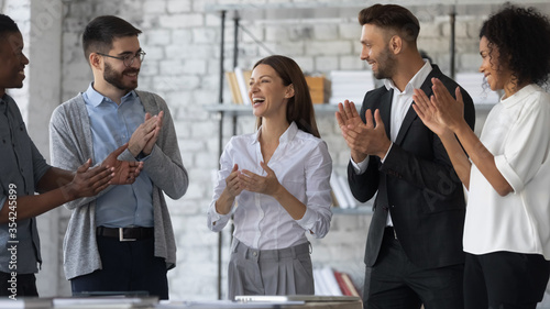 Friendly diverse employees congratulating businesswoman with business achievement, great work results or job promotion, business people applauding and cheering, standing in modern office photo