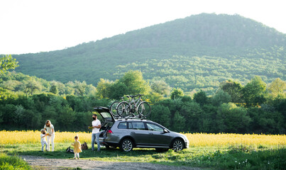 Family with two small children and face masks going on cycling trip in countryside.