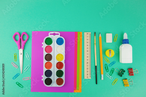 School supplies, top view of scissors, paper, watercolour paintings, brush, pen and ruler on the green background