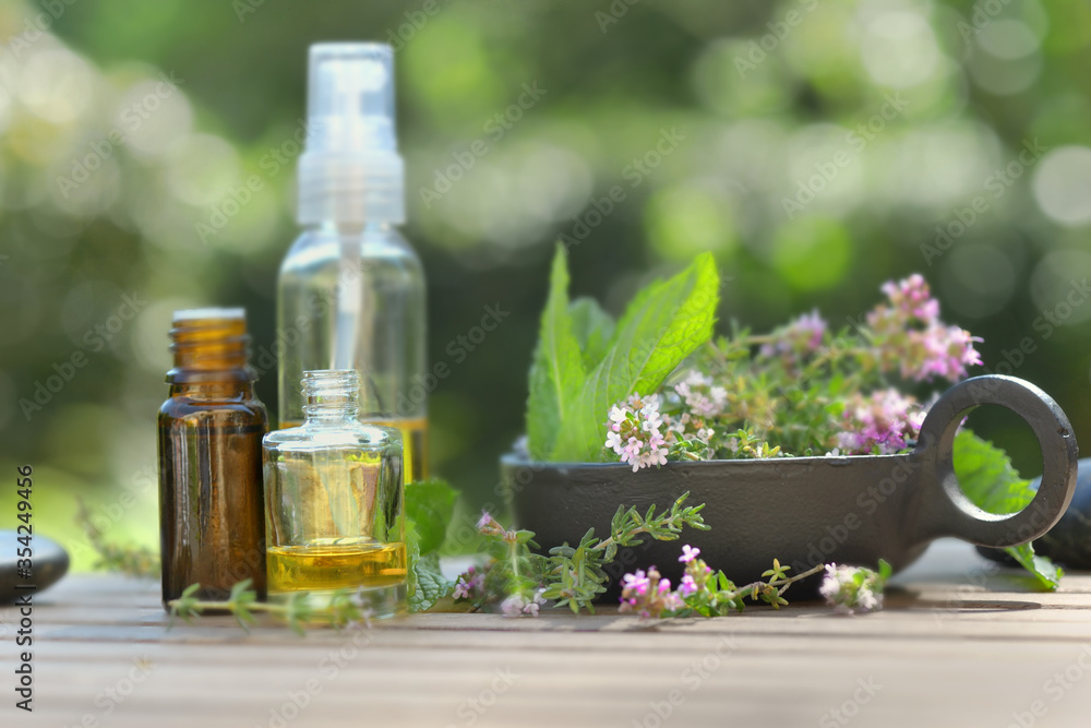 bottles of essential oil and flowers of aromatic herb on a table and on green background bottles of essential oil and flowers of aromatic herb on a table and on green background