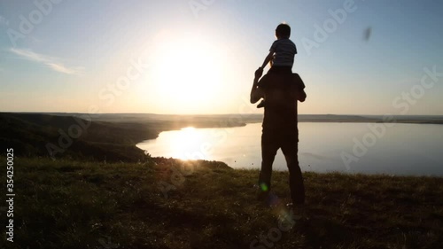 Silhouettes of people at sunset. Dad and little son play and enjoy the sunset on the rock against the backdrop of the sunset on the shore of a mountain lake, sea or ocean.