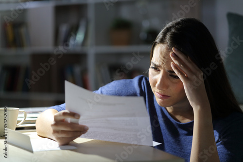 Worried girl reads bad news on letter at night at home