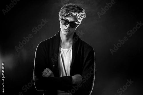Trendy young man with cool hairstyle wearing black jacket with sunglasses. High Fashion male model posing on black background. Art design concept