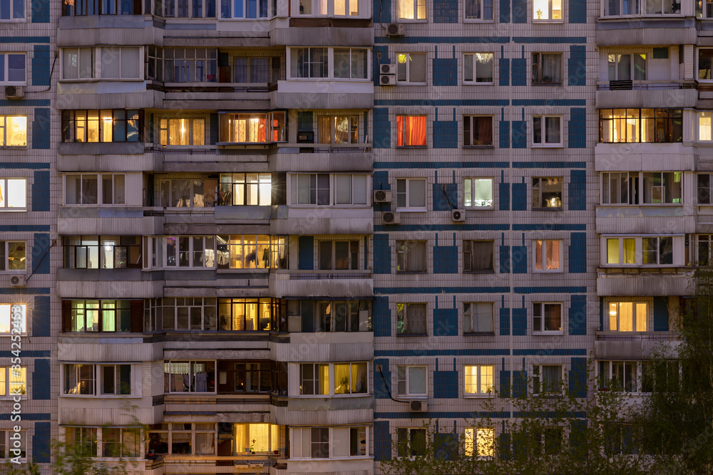 Facade of large multi-storey block residential buildinf with many bright lighting windows in apartments and balconiesю Evening view. Moscow Russia