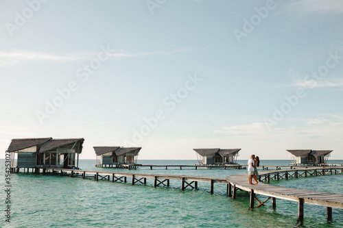 Happy loving couple in white clothes posing on a pier on Maldives. Couple in white on a tropical beach jetty at Maldives. Honeymoon  on the ocean © Yevhenii