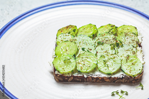 Cucumber and cream cheese toast on white plate, top view. Healthy vegetarian diet concept.