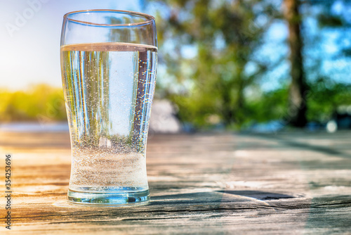 tall transparent glass with water on a wooden surface on a background of a summer landscape, blurred background
