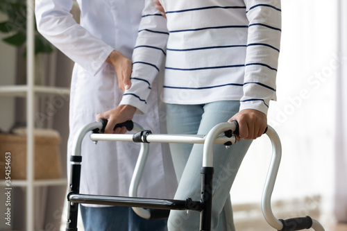 Cropped image caregiver helping to disabled patient walking with rollator equipment reduce load and joint pain with arthritis. Physical therapist and therapy, neurological cerebellar disorders concept photo