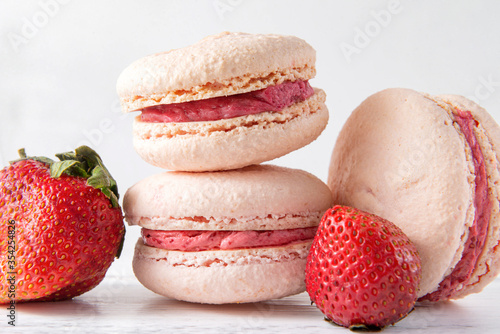 3 cookies with strawberry, beige French macaroons  with  pink cream on a white wooden background