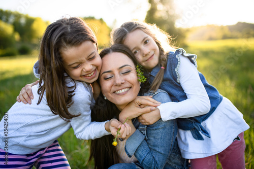 Mother with two small daughters having fun outdoors in spring nature, hugging.