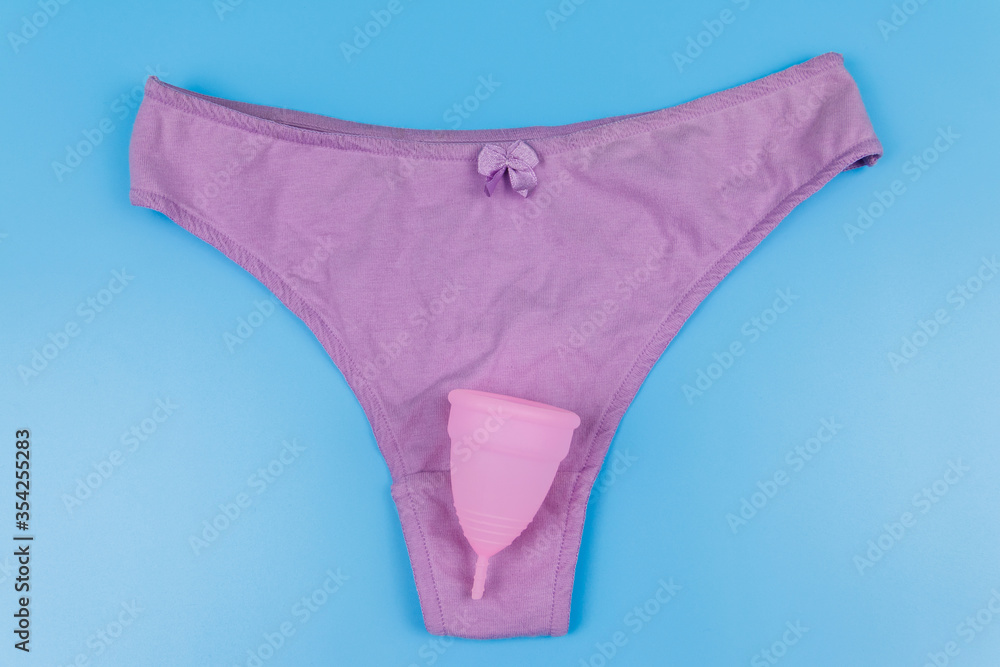 Women's panties with menstrual cup on pastel blue background. Top view. Concept of critical days, menstruation, feminine hygiene Women's panties with menstrual cup on pastel blue background. Top view. Concept of critical days, menstruation, feminine hygiene