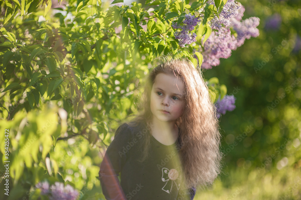 Outside portrait of a beautiful girl with long curly hair near lilac bushes Outside portrait of a beautiful girl with long curly hair near lilac bushes