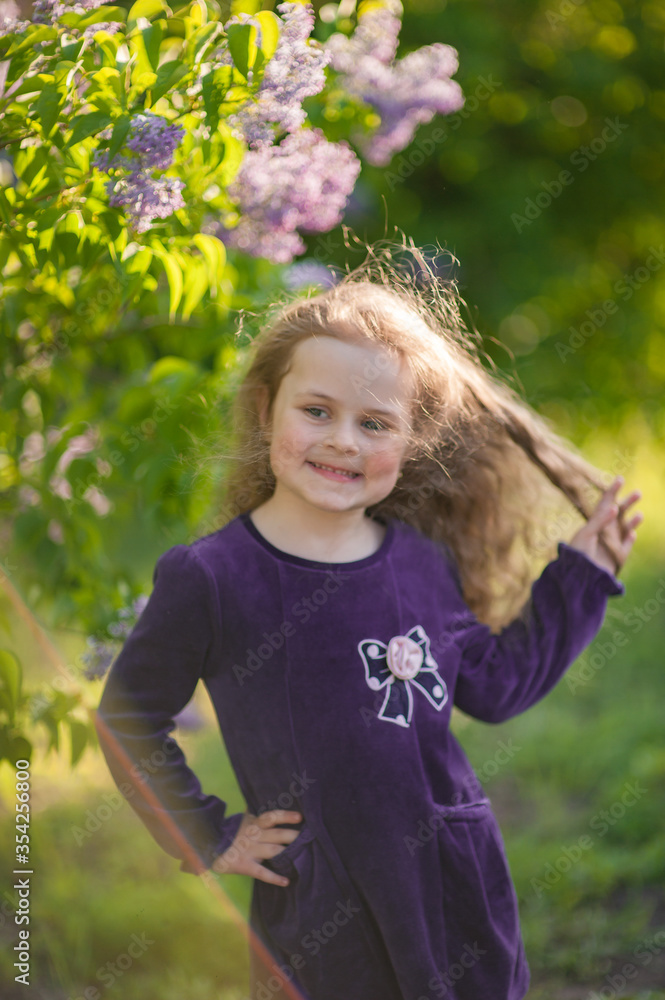 Outside portrait of a beautiful girl with long curly hair near lilac bushes Outside portrait of a beautiful girl with long curly hair near lilac bushes