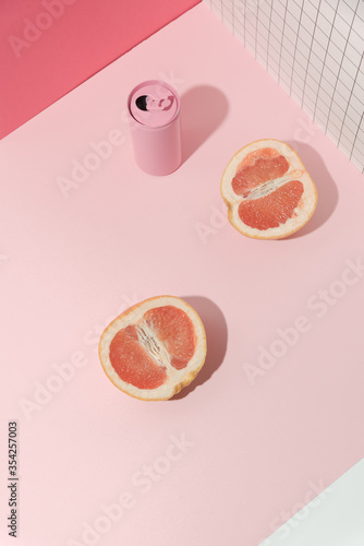 Pink aluminum soda-can and halves of grapefruit on a light pink surface and pink geometric background. Direct hard light