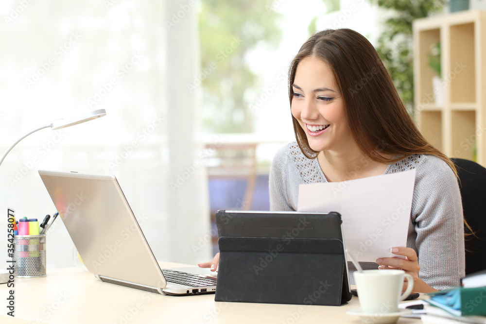 Woman with laptop and tablet compares document at home Woman with laptop and tablet compares document at home