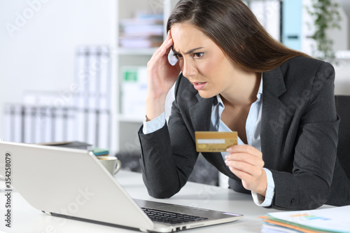 Worried executive paying with card on laptop at office