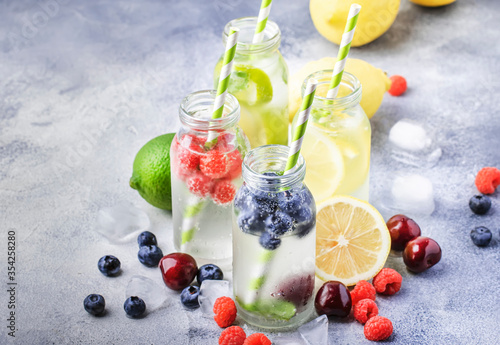 Bilde på lerret Berry and citrus fruit infused summer cold drinks in glass bottles on gray stone