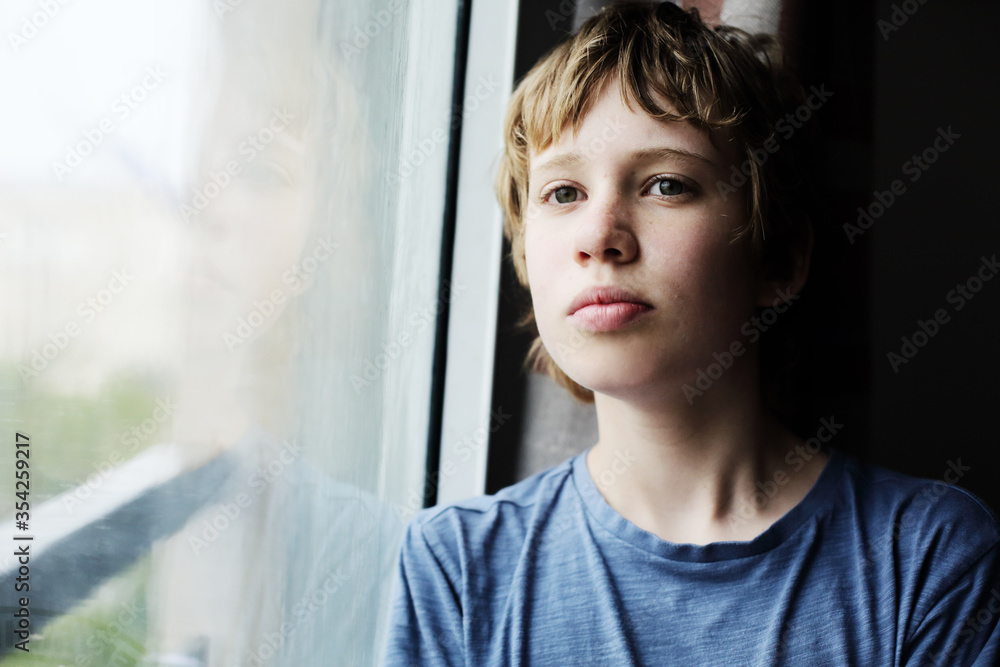 Cute 12 years old autistic boy looking through the window