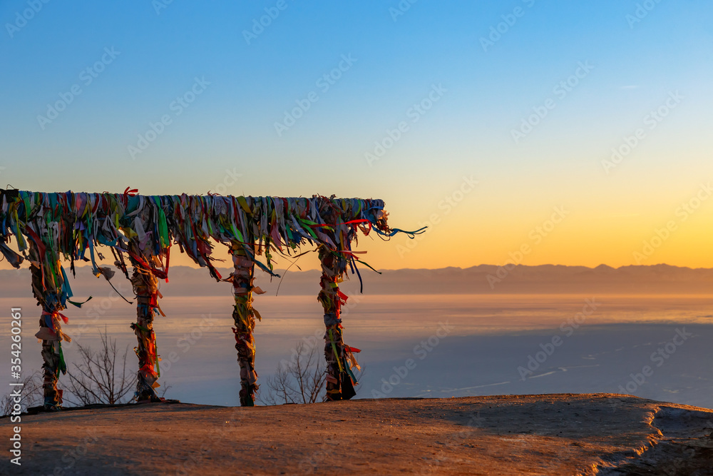 View at Baikal lake at sunset in winter with fence covered with religious colorful ribbons