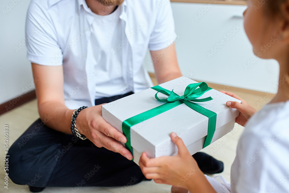 Little girl is giving her handsome father a gift box on Father's day, smiling daughter congratulating dad and giving present on birthday at home. I love you, dad. Happy Father's Day.. Little girl is giving her handsome father a gift box on Father's day, smiling daughter congratulating dad and giving present on birthday at home. I love you, dad. Happy Father's Day..