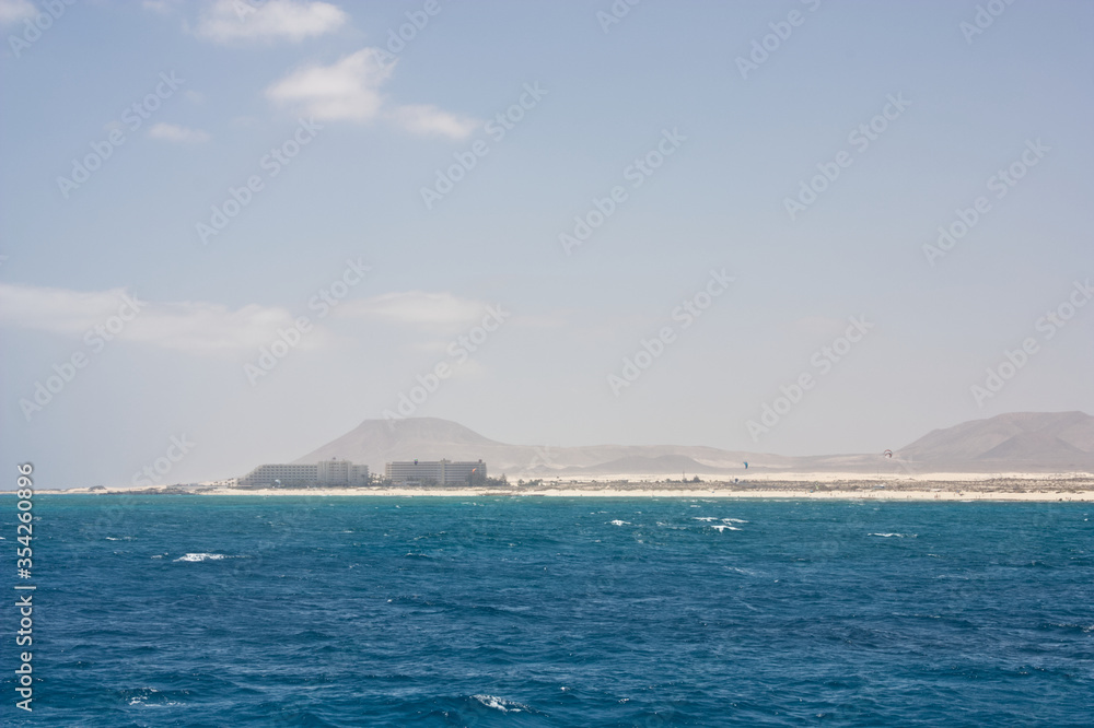 Seascape with white capped waves and fluffy clouds looking toward the Las Dunas area of Corralejo Fuertaventura from the sea. Space left for copy text