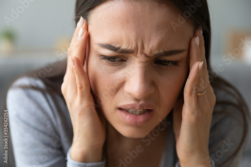 Fényképezés Close up view frown face of unhealthy 20s woman touches temples with hands suffe