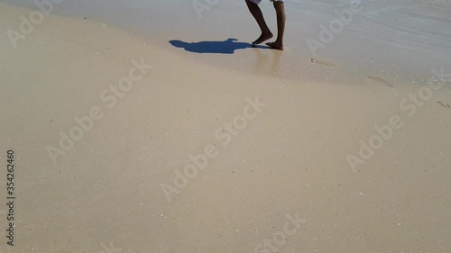 Man stepping at the white sand at sea beach. Legs walking near ocean. Bare foot going on sandy shore with waves. Summer vacation or holiday. Closeup.