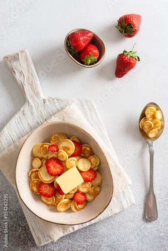 Bowl with tiny pancake cereal with strawberries on a white concrete background. Trendy food. Mini cereal pancakes. Trendy breakfast during quarantine. Top view, close up