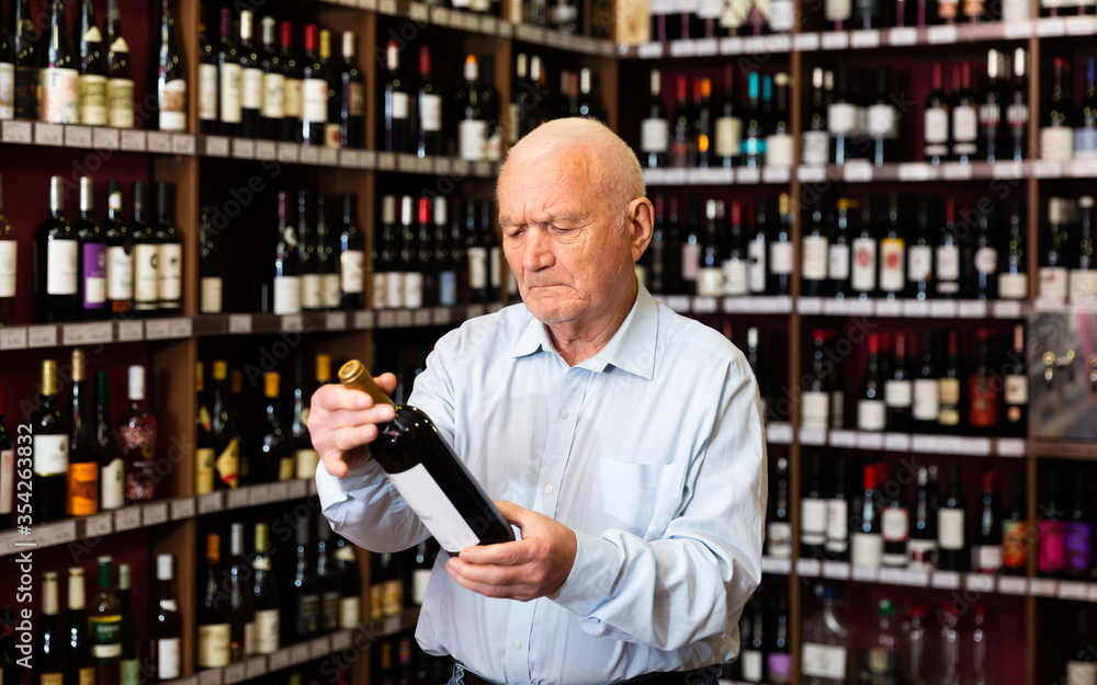 Attentive pensioner chooses red wine in a liquor store