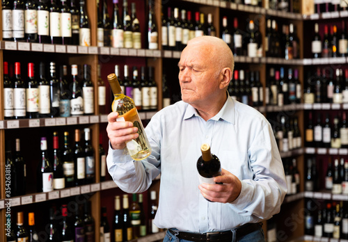 Serious elderly man chooses between red and white wine in a liquor store