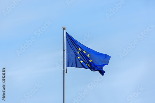 European flag with yellow stars for each member state on a blue background waving in the wind against a bright sky, large copy space on all sides, partly motion blur
