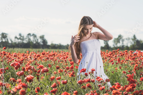 A girl in a white sundress enjoys the warmth of the sun and walks through a poppy field