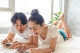 Happy Asian couple is playing mobile game together on their bed.