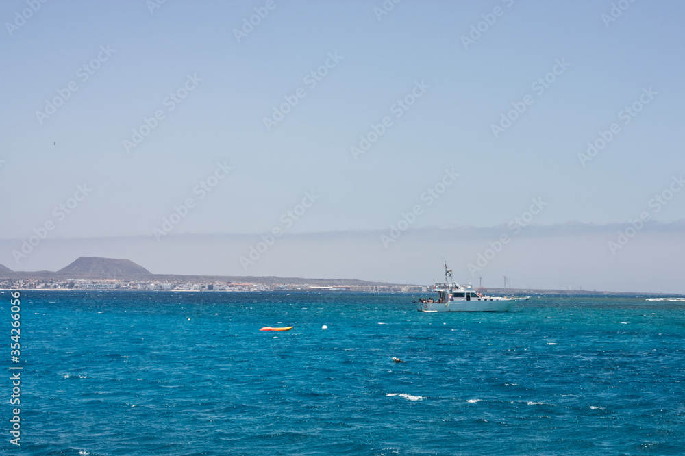 Seascape with white capped waves, a dive boat and blue sky looking towards Corralejo Fuertaventura from the sea. Space left for copy text